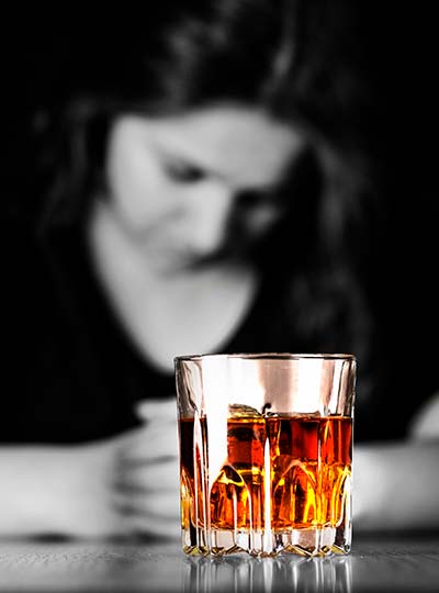 стакан с алкоголем на фоне грустной женщины
